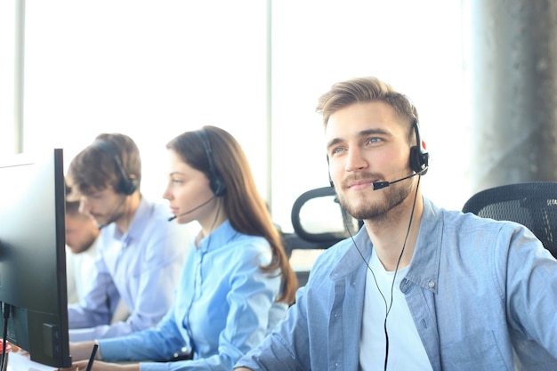 Retrato de trabajador de call center acompañado de su equipo. Operador de soporte al cliente sonriente en el trabajo.