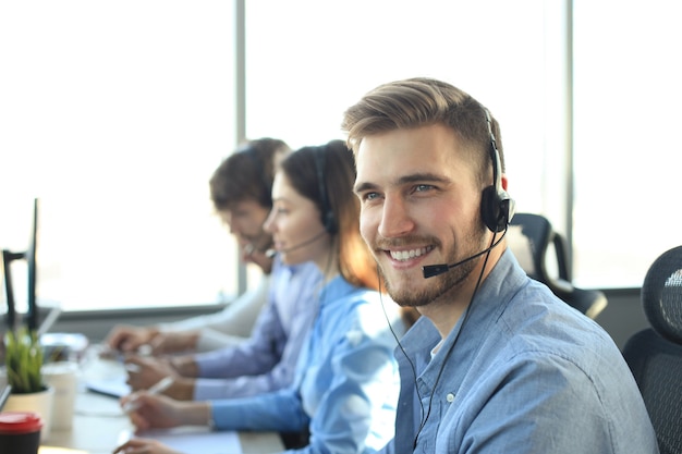 Retrato de trabajador de call center acompañado de su equipo. Operador de soporte al cliente sonriente en el trabajo.