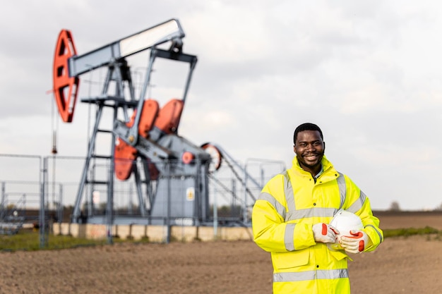 Foto retrato de un trabajador del campo petrolero en ropa de trabajo protectora de pie frente a una plataforma petrolera