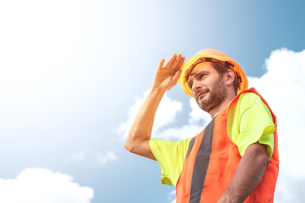 Un retrato de un trabajador se para con confianza en un traje de trabajo naranja y un casco de seguridad contra el cielo Concepto de trabajo de trabajador industrial inteligente