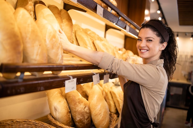 Retrato de un trabajador de delicatessen que organiza pasteles frescos y criados en el departamento de panadería del supermercado