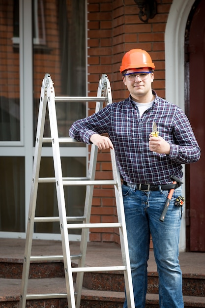 Retrato de trabajador feliz en sitio de construcción sosteniendo Thumbs up