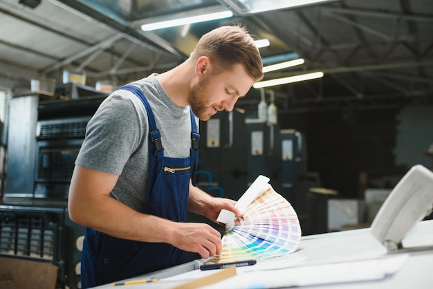 Foto retrato del trabajador de la línea de producción que controla el proceso de fabricación de la máquina industrial de embalaje moderna en la fábrica de impresión
