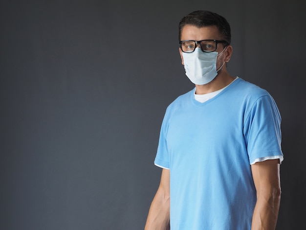 Retrato de un trabajador médico usa mascarilla y gafas mirando a cámara, con espacio de copia. Fondo gris