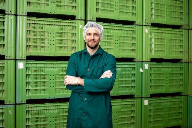 Retrato de trabajador de pie junto a cajas de fruta de manzana en el almacén de la fábrica de alimentos orgánicos.