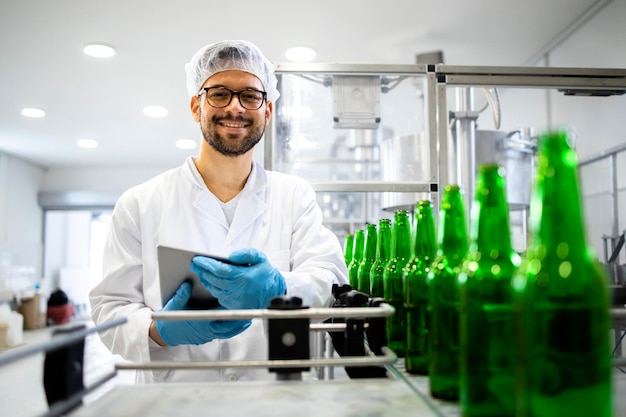 Retrato de un trabajador tecnólogo de pie en una fábrica de embotellado de cerveza comprobando la calidad del producto