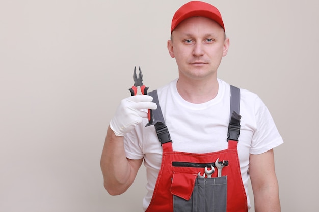 Retrato, de, un, trabajador, en, uniforme rojo, gorra, y, guante blanco, tenencia, alicates