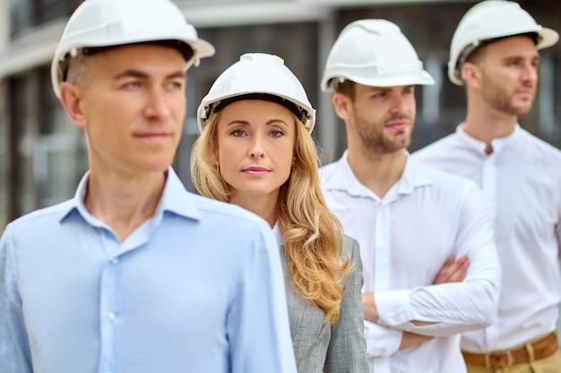 Retrato de una tranquila dama encantadora inspectora rodeada de trabajadores de la construcción masculinos en cascos de seguridad mirando hacia el futuro