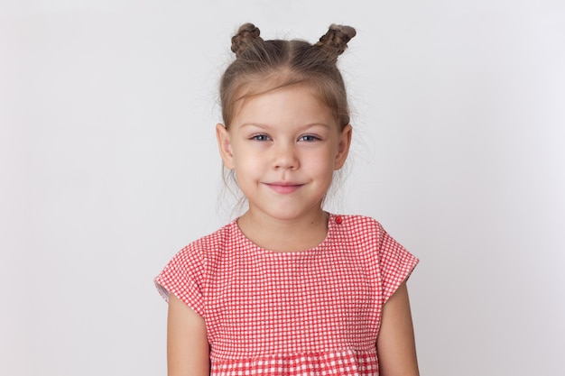 Retrato de una tranquila niña caucásica de cinco años de edad en el fondo blanco mirando a la cámara