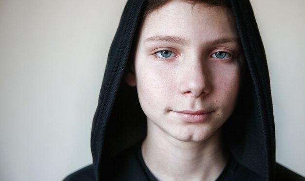 Retrato de un tranquilo adolescente de ojos azules en una capucha negra