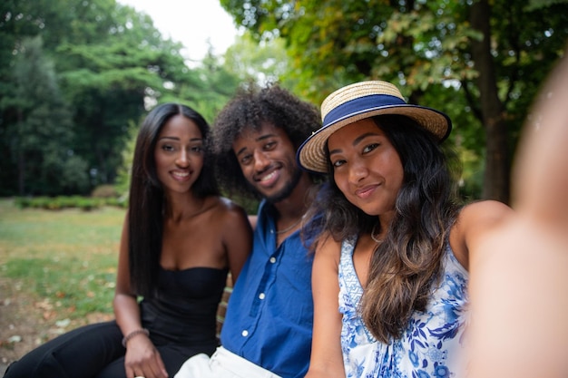 Retrato de tres amigos sonrientes sentados en un banco tomando un selfie en un parque público