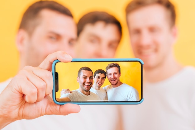 Foto retrato de tres amigos varones tomando selfie en smartphone