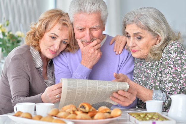 Retrato de tres ancianos desayunando y leyendo un periódico