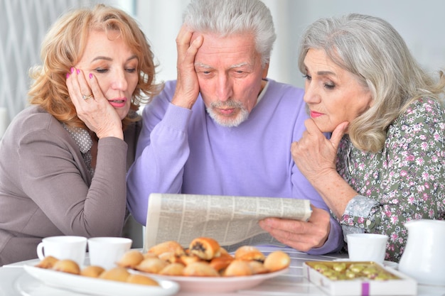 Retrato de tres ancianos desayunando y leyendo un periódico