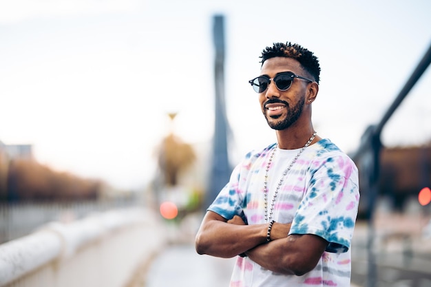 Retrato de tres cuartos de un hombre afroamericano sonriente con una camiseta colorida y gafas de sol con los brazos cruzados