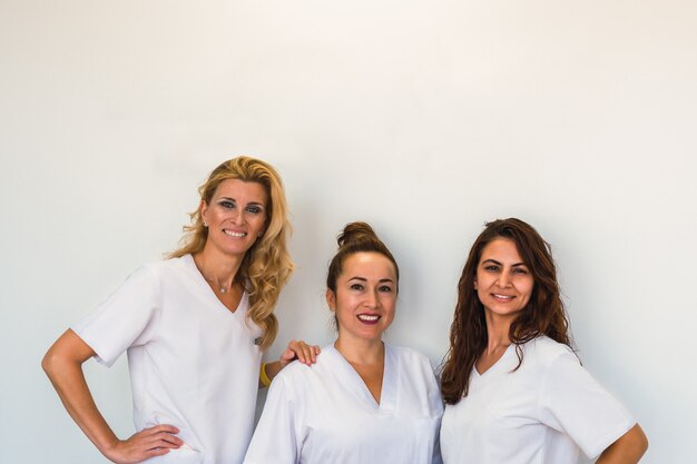 Retrato de tres esteticista posando y mirando a cámara sobre una pared blanca en el salón de spa.