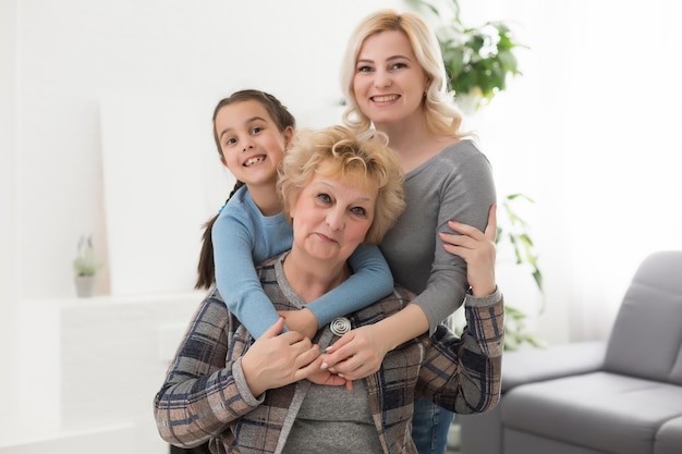 Foto retrato de tres generaciones de mujeres miran la cámara posando para una foto familiar, linda niña abrazan a mamá y abuela disfrutan del tiempo en casa, sonrientes madre, hija y abuela pasan el fin de semana juntas