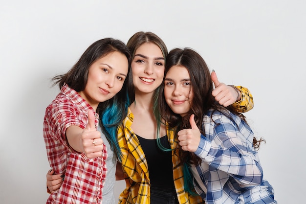 Retrato de tres hermosas mujeres jóvenes felices sonriendo alegremente mostrando los pulgares para arriba en blanco