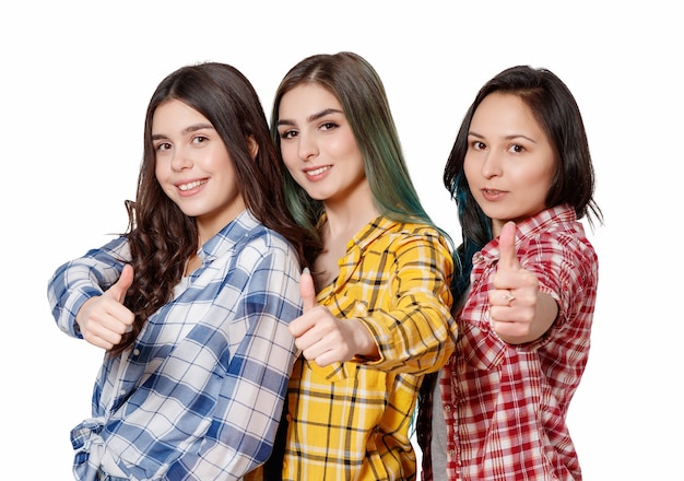 Retrato de tres hermosas mujeres jóvenes felices sonriendo con alegría mostrando los pulgares para arriba aislados en blanco