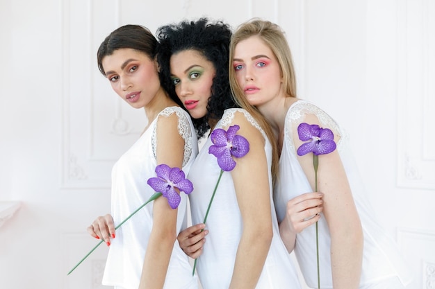 Retrato de tres hermosas mujeres jóvenes multirraciales con diferentes tipos de piel Niñas de pie en fila y mirando en direcciones opuestas Concepto de diversos amigos sosteniendo una flor de orquídea