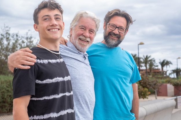 Retrato de tres hombres que se ríen, abuelo, hijo y nieto, permanecen juntos al aire libre sonriendo