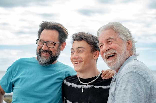 Retrato de tres hombres que se ríen, abuelo, hijo y nieto, permanecen juntos en la playa sonriendo