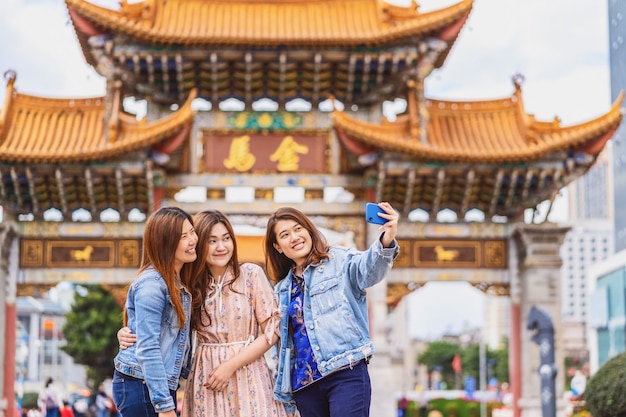 Foto retrato tres mujeres asiáticas de felicidad usando un teléfono móvil inteligente para autofoto juntos, kunming, china