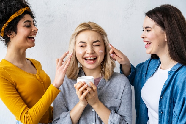 Retrato de tres mujeres felices riendo y jugando con crema hidratante