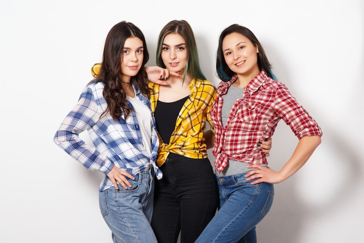 Foto retrato de tres mujeres jóvenes hermosas chicas delgadas en camisas a cuadros rojo, amarillo y azul. en la pared blanca