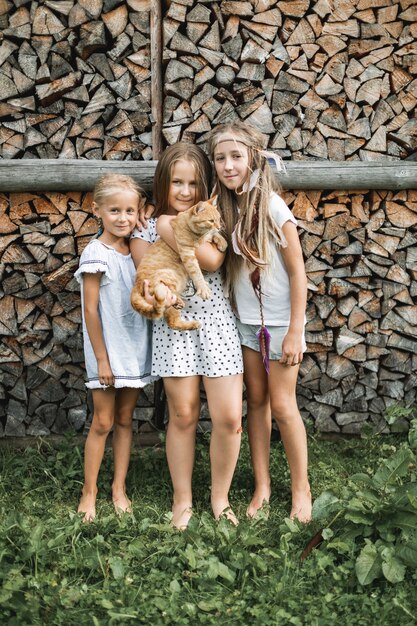 Retrato de tres niñas bonitas, hermanas, en ropa casual, de pie juntos en el fondo de leña apilada al aire libre