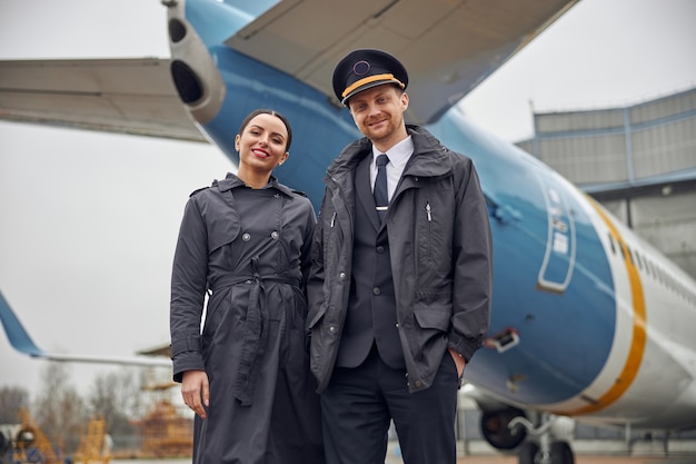 Retrato de la tripulación del avión caucásico seguro feliz cerca del avión