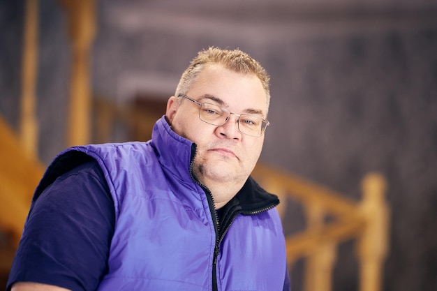 Retrato de un triste hombre con sobrepeso con gafas y chaqueta sin mangas en casa