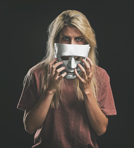 Foto retrato triste y mujer con máscara bipolar para ocultar la lucha contra la depresión con maqueta en el estudio chica deprimida que oculta emociones de identidad y trastorno de salud mental con disfraz de cara de teatro