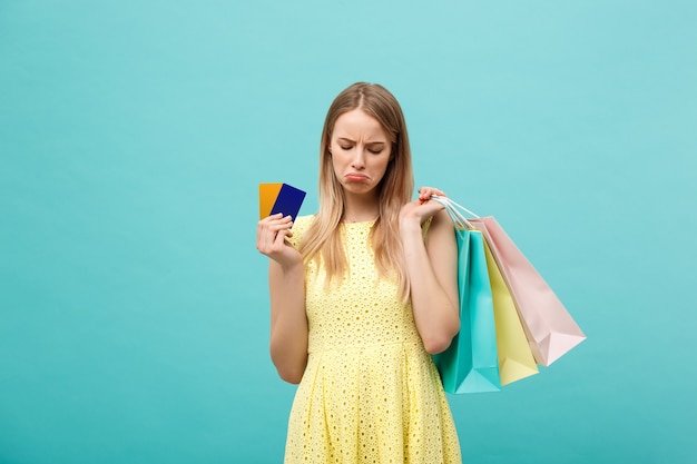 Retrato, de, un, triste, mujer, tenencia, bolsas de compras, y, tarjeta bancaria, aislado, en, un, fondo azul