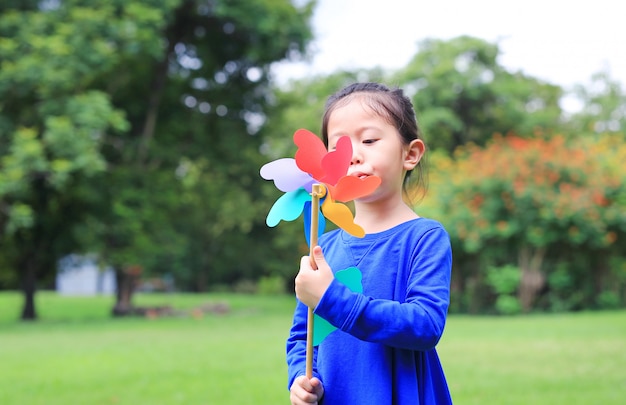 Retrato de la turbina de viento de la pequeña muchacha asiática del niño que sopla en el jardín del verano.