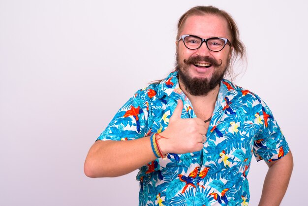 Retrato de turista barbudo con sobrepeso hombre con bigote y cabello largo vistiendo camisa hawaiana contra la pared blanca