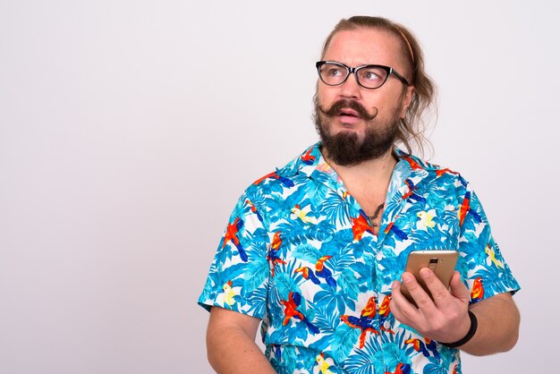 Retrato de turista barbudo con sobrepeso hombre con bigote y cabello largo vistiendo camisa hawaiana contra la pared blanca