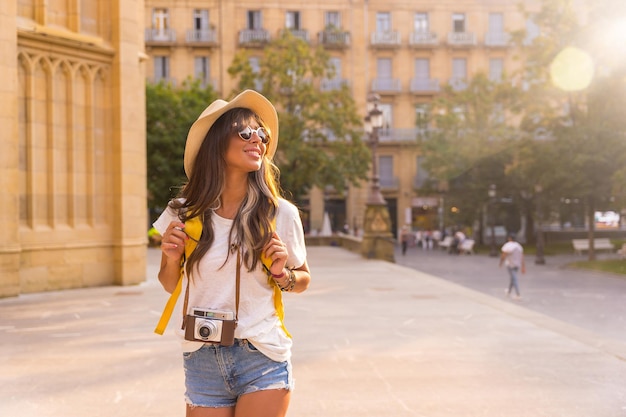 Retrato de un turista con un sombrero de viaje en la cámara fotográfica al atardecer en la ciudad al lado de una iglesia