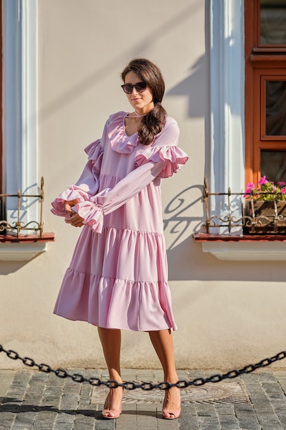 Retrato urbano al aire libre de joven hermosa chica elegante en vestido rosa de gran tamaño