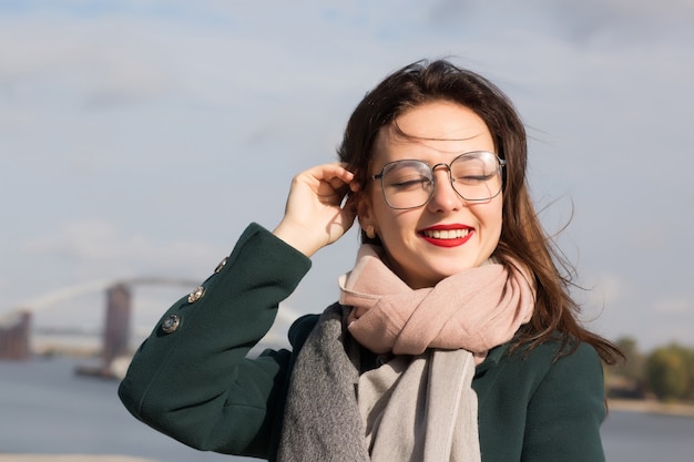 Retrato urbano de uma linda senhora morena posando para a cidade, usando óculos, casaco verde e lenço