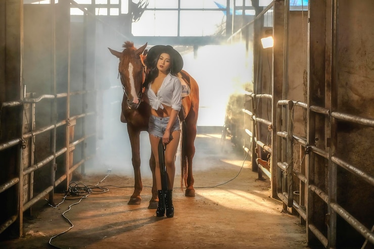 Foto retrato de una vaquera con un caballo de pie en el establo