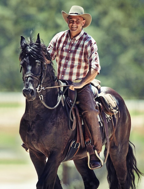 Retrato de vaquero y hombre montando caballo con silla en el campo para la equitación o el entrenamiento El verano de la naturaleza y la sonrisa con un jinete maduro a caballo en un animal en un rancho al aire libre en la zona rural de Texas