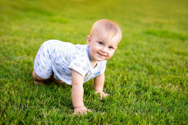 Retrato del verano del bebé divertido feliz al aire libre en hierba en campo. Niño aprendiendo a gatear