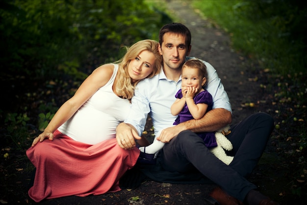 Retrato de verano de familia feliz. Madre embarazada, padre e hija pequeña.