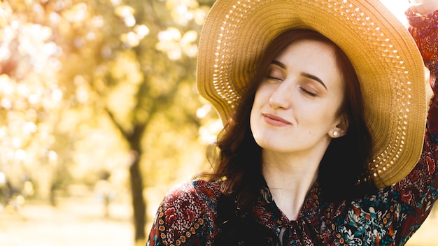 Retrato de verano, hermosa joven con sombrero de paja al atardecer en el jardín