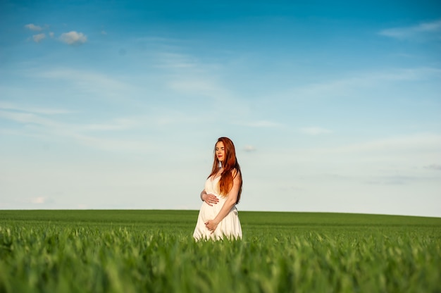 Retrato de verano hermosa mujer embarazada caminando en campo verde