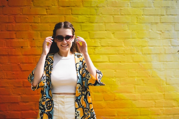 Retrato de verano de mujer joven sonriente feliz con gafas de sol sobre fondo naranja colorido