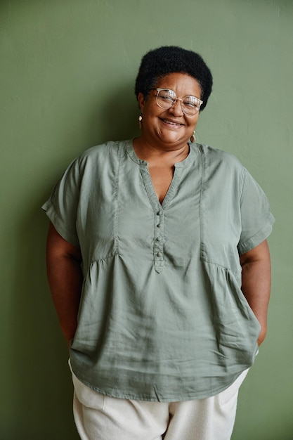 Retrato vertical de una anciana negra con gafas y sonriendo a la cámara mientras se enfrenta a un fondo verde