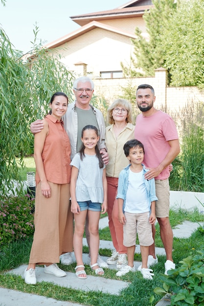 Retrato vertical completo de uma família de várias gerações de seis pessoas, em pé no quintal em um dia ensolarado de verão