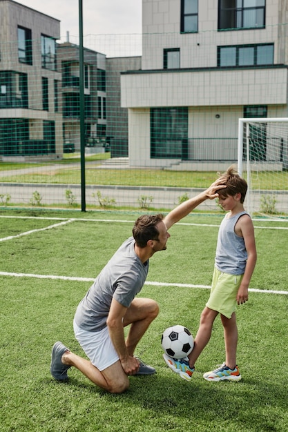 Retrato vertical de amoroso pai e filho jogando futebol juntos na quadra ao ar livre